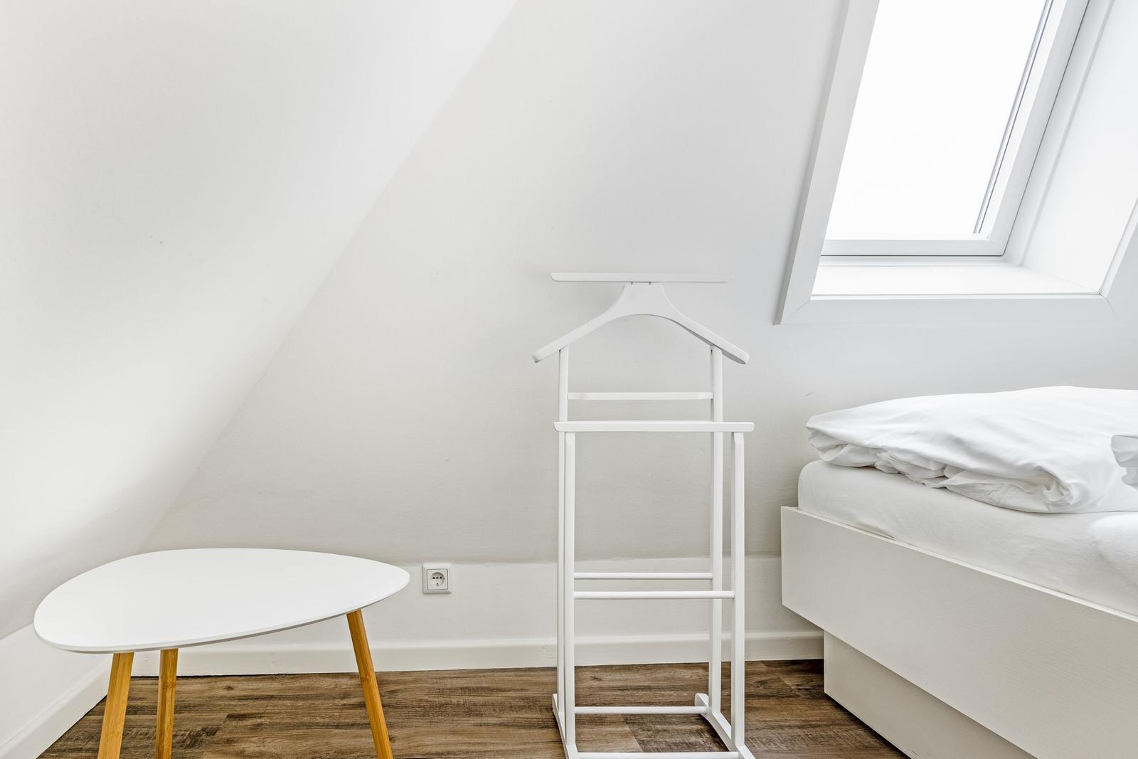 Bedroom with sloped ceiling, bed, coat stand, and table.