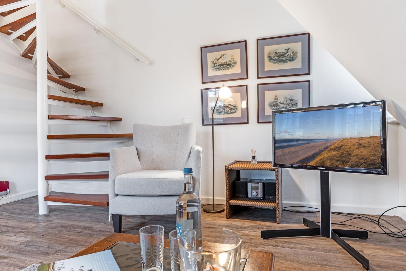 Living area with armchair, TV, and staircase.