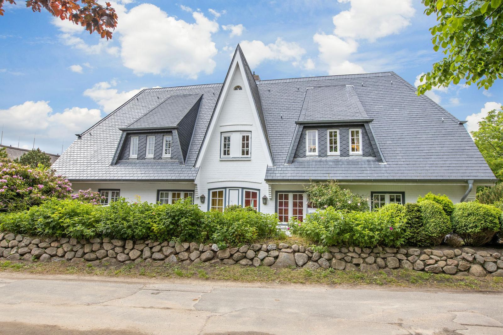 A white house with a gray roof and green surroundings.