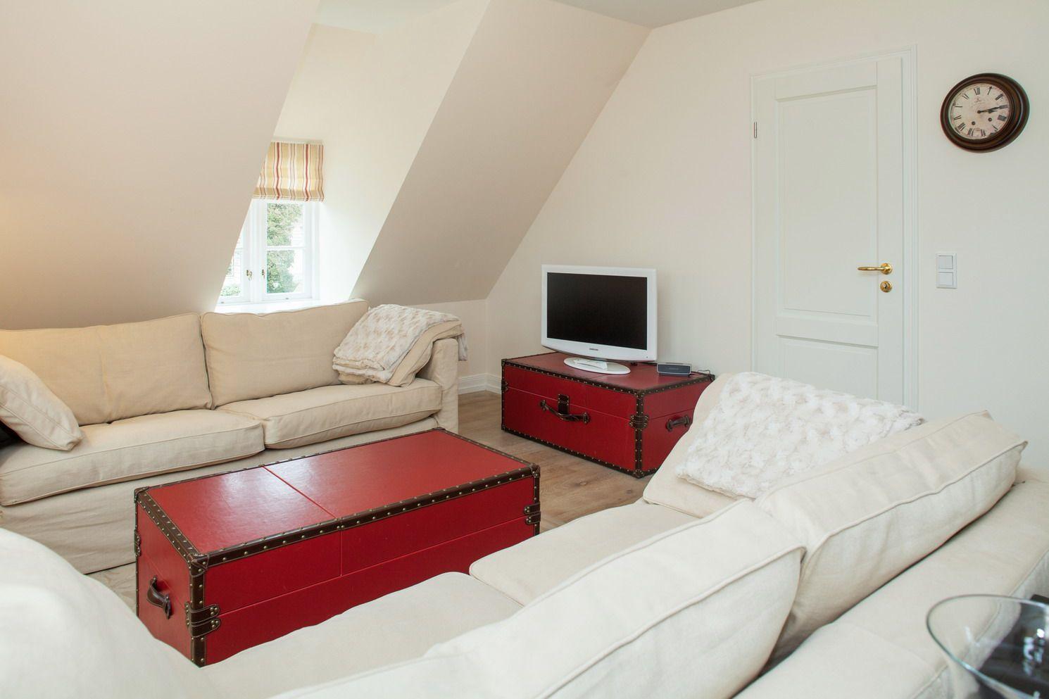 Living room with cream sofas, red trunk table, and TV on red trunk.