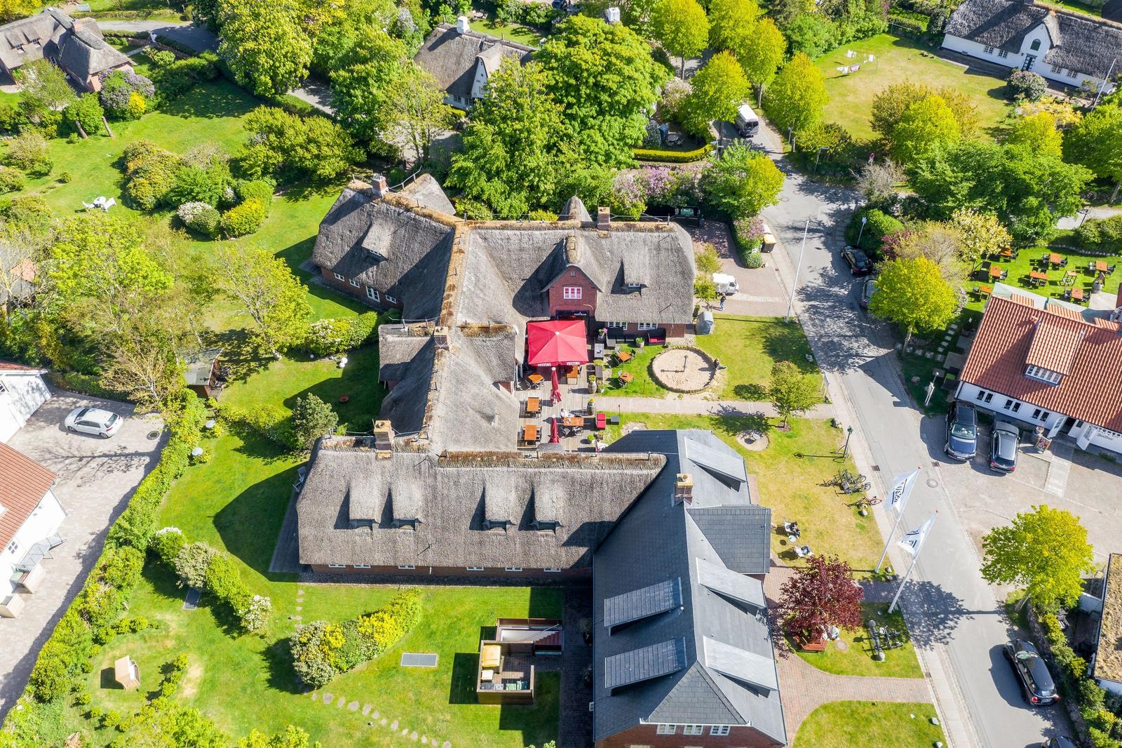 Village house with thatched roof, garden, and terrace with red umbrella.