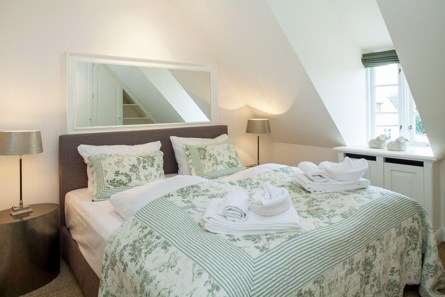 Bedroom with sloped ceiling, bed with green-and-white coverlet, and window with view outside.