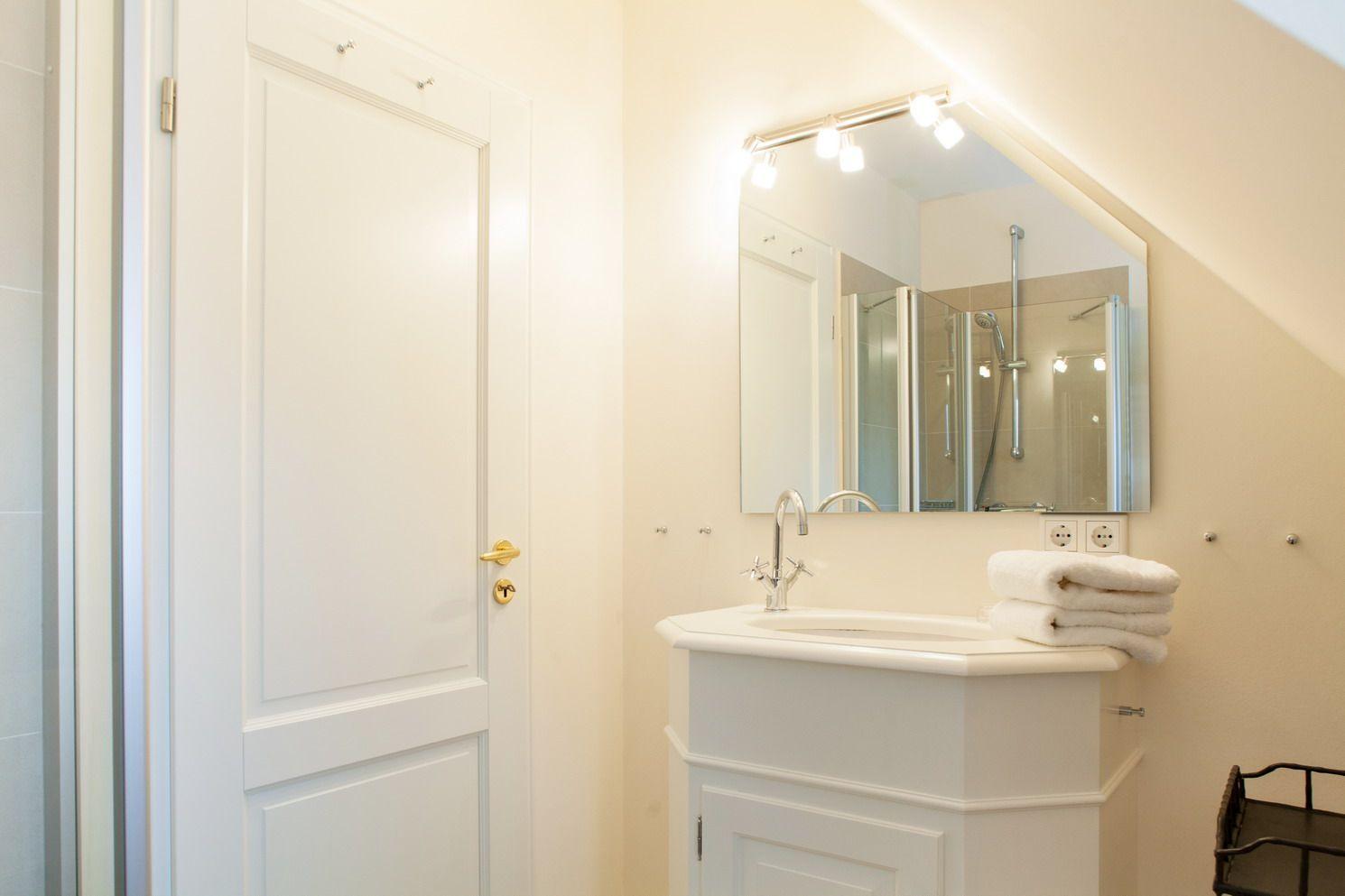 Bathroom with sink, mirror, and shower under sloped ceiling.