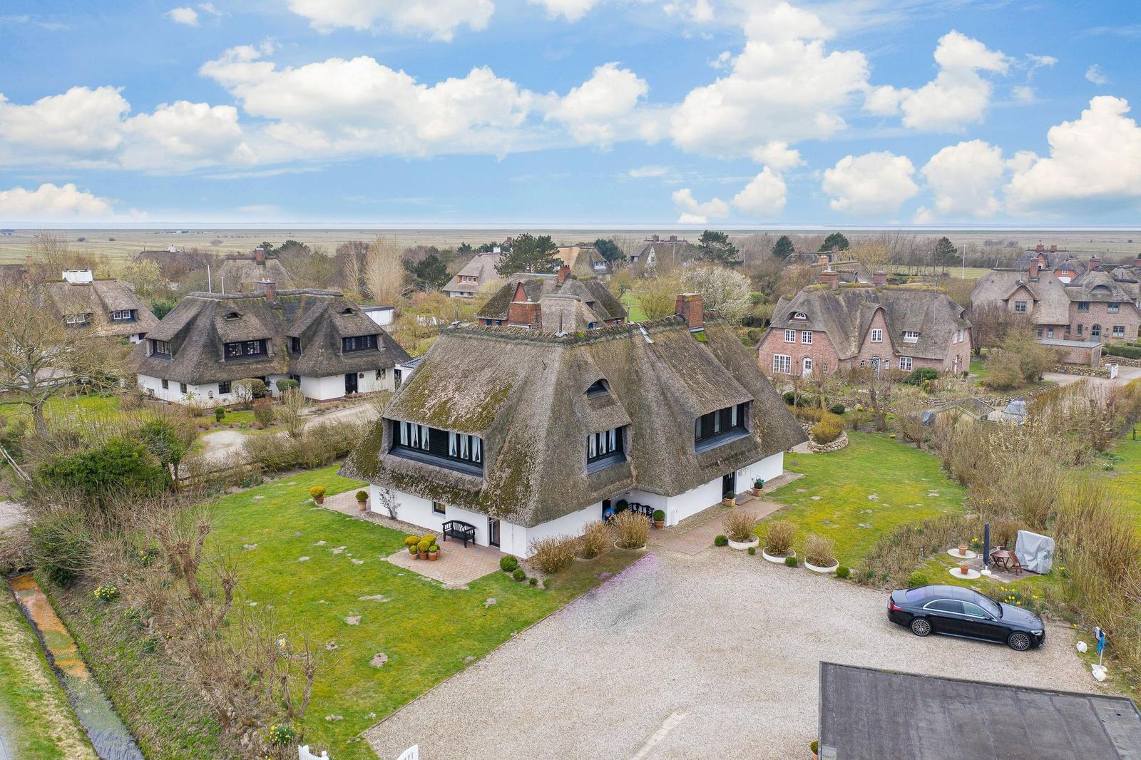 Haus mit Strohdach, Garten und Parkplatz. Blick auf Dorf und Landschaft.