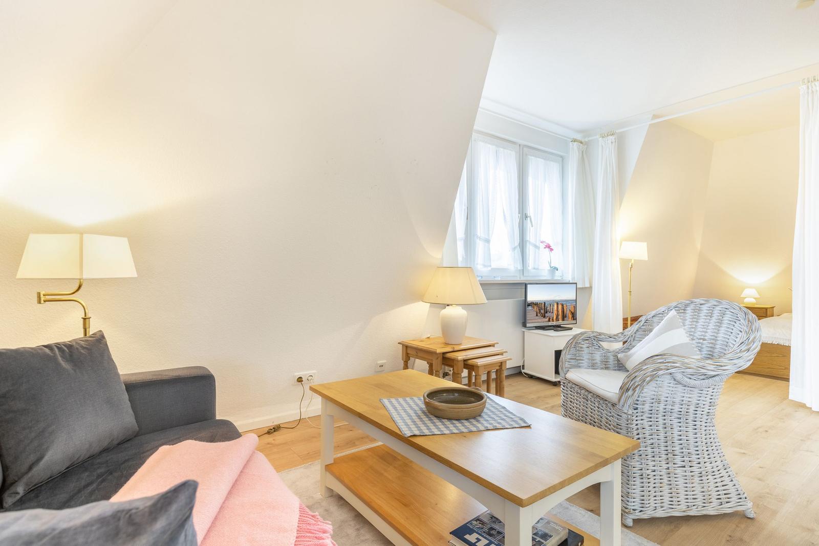 Wohnzimmer mit Sofa, Esstisch und Fernseher. Blick in Schlafzimmer mit Bett.