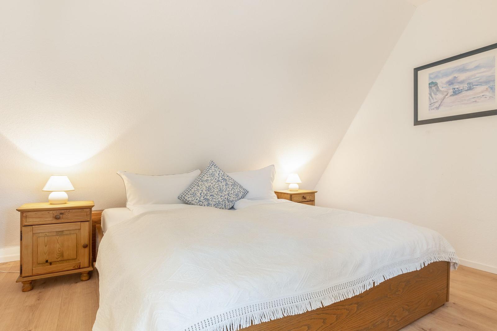Schlafzimmer mit Doppelbett, zwei Nachttischen und einer Wanddekoration.