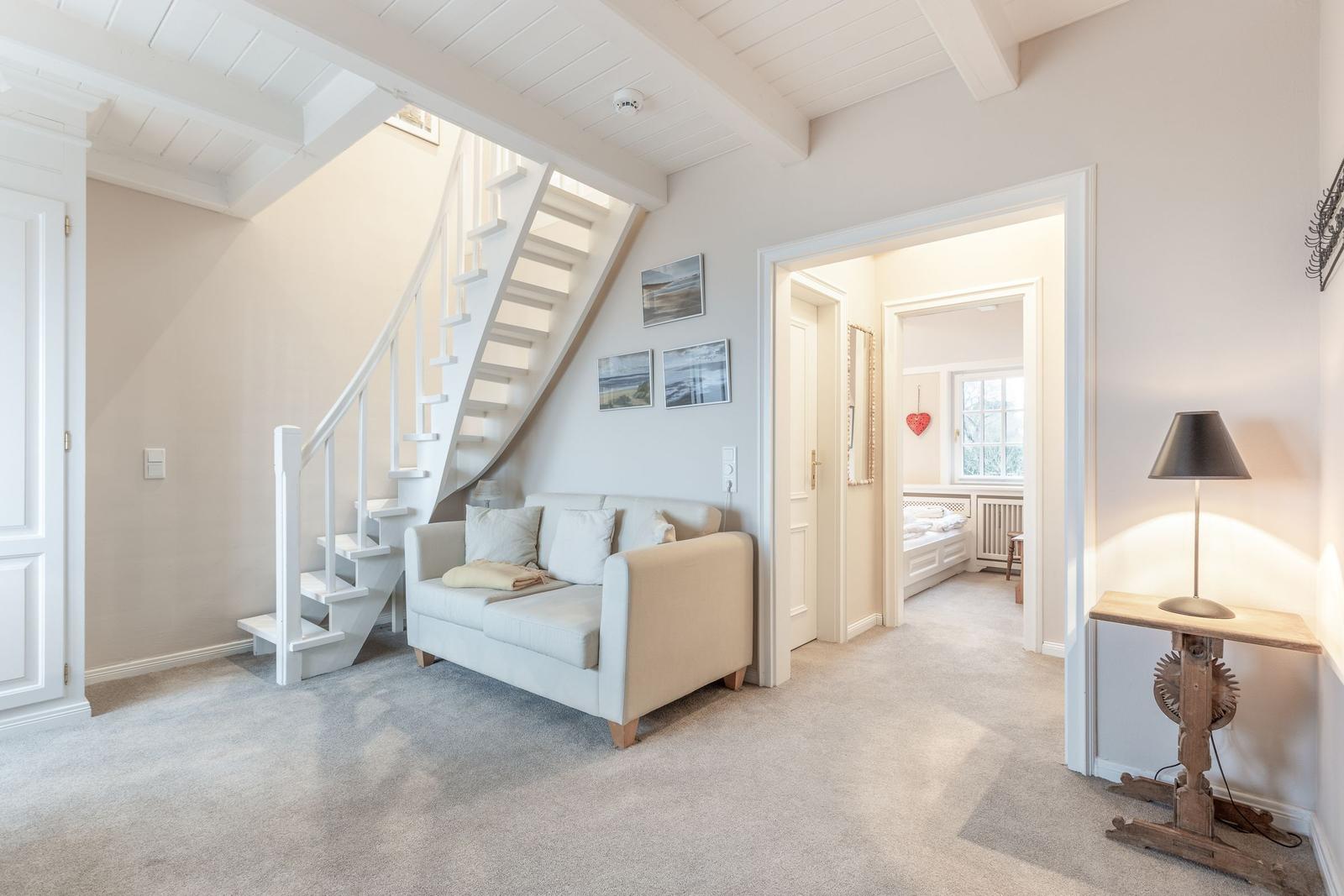 Wohnbereich mit Sofa, Treppe und Blick in Schlafzimmer.
