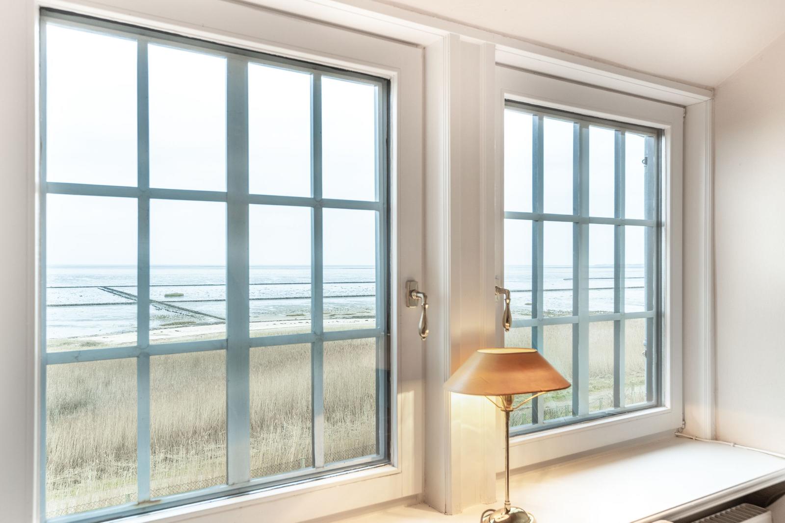 Zwei Fenster mit Meerblick und einer Stehlampe auf Fensterbank.