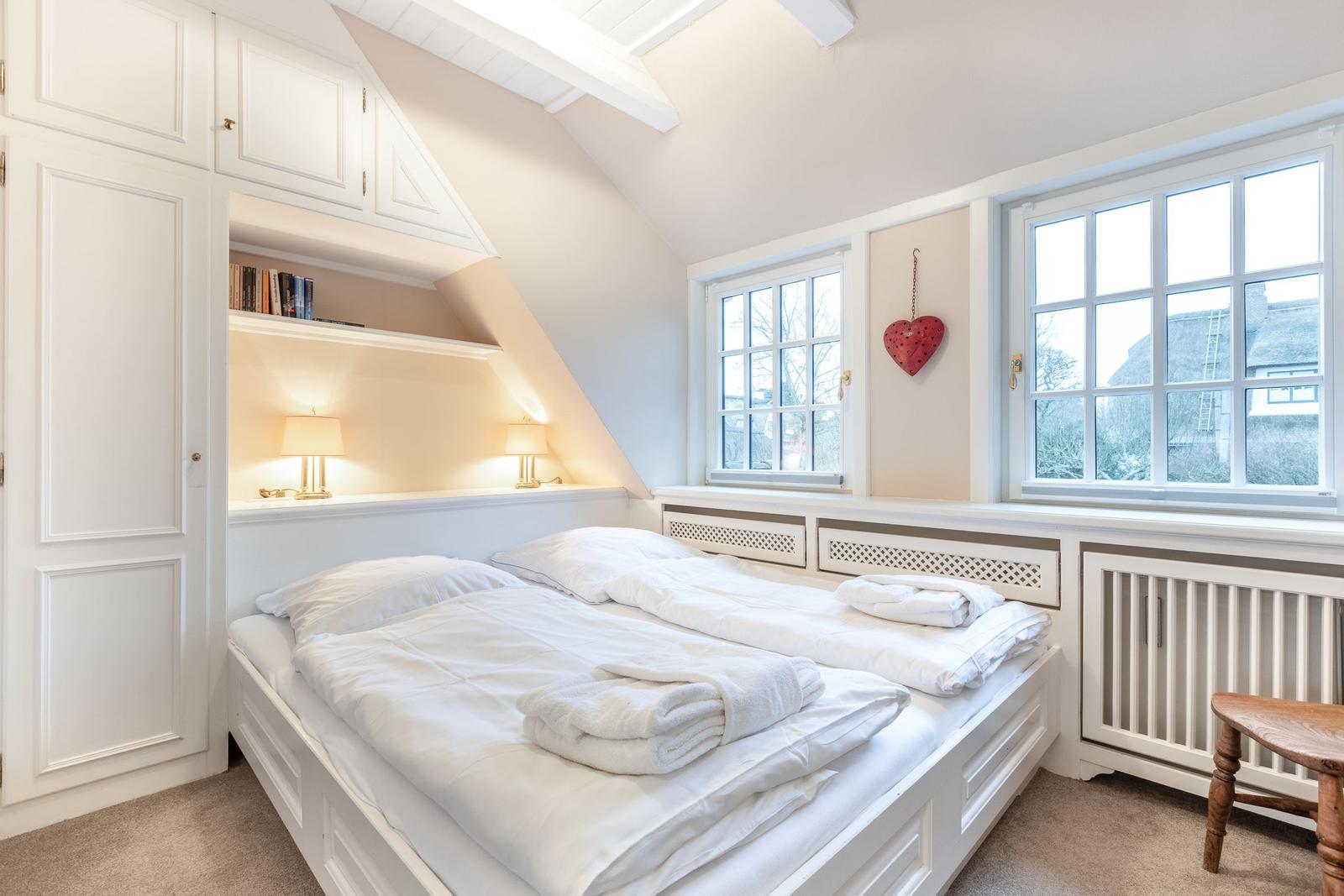 Schlafzimmer mit Doppelbett, weißen Möbeln und Fenstern mit Blick nach draußen.