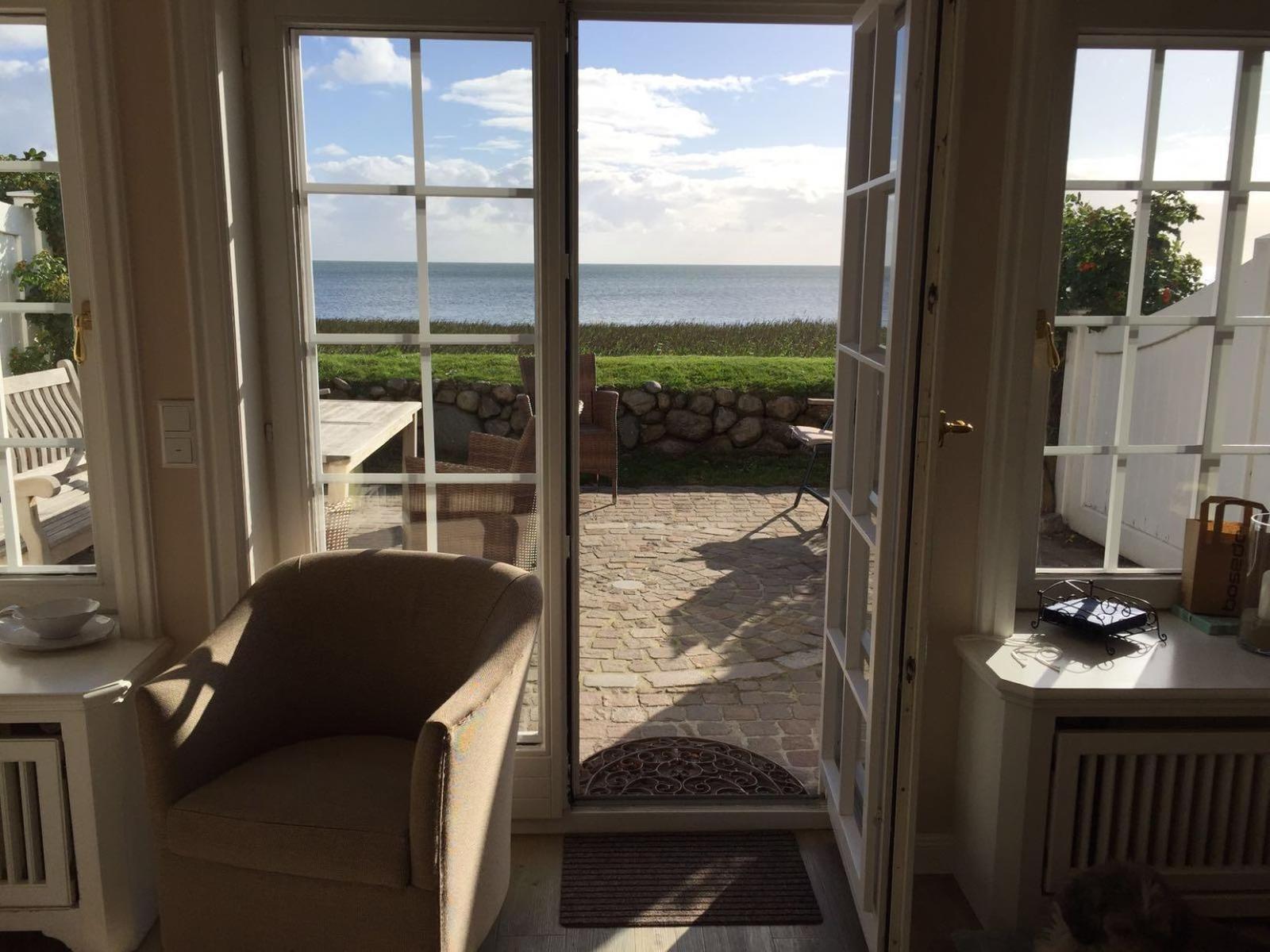 Durch offene Türen blickt man auf einen gepflasterten Hof mit Garten und Meer.