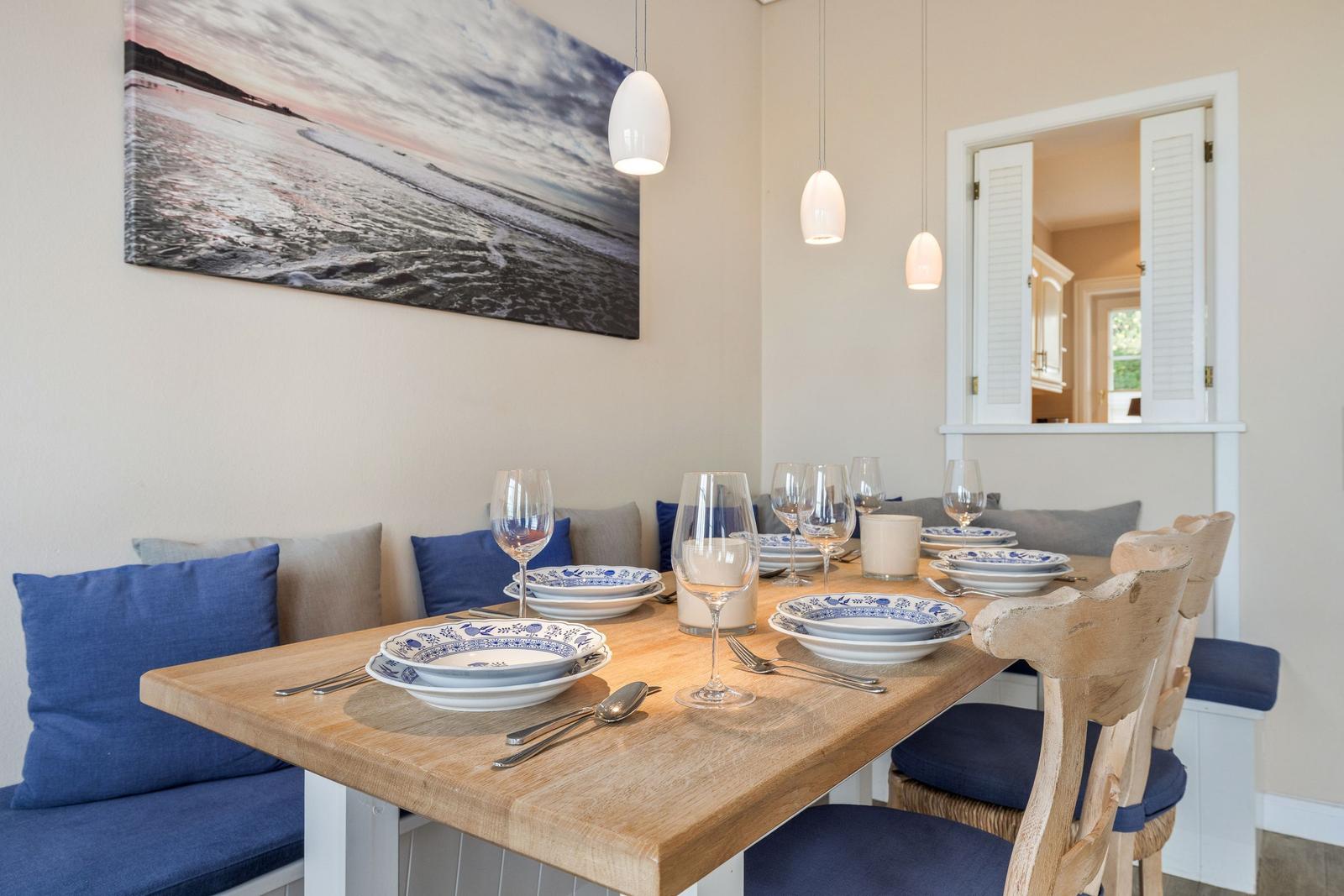 Esstisch mit blauem Geschirr und Holzstühlen. Wandbild und Hängelampen.