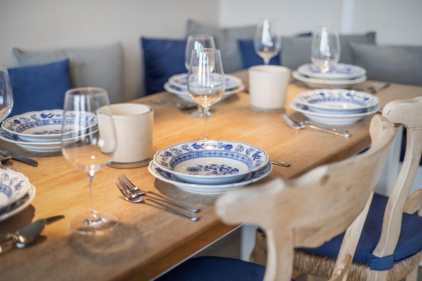 Holztisch mit blau-weißem Geschirr und Stühlen mit blauen Kissen.
