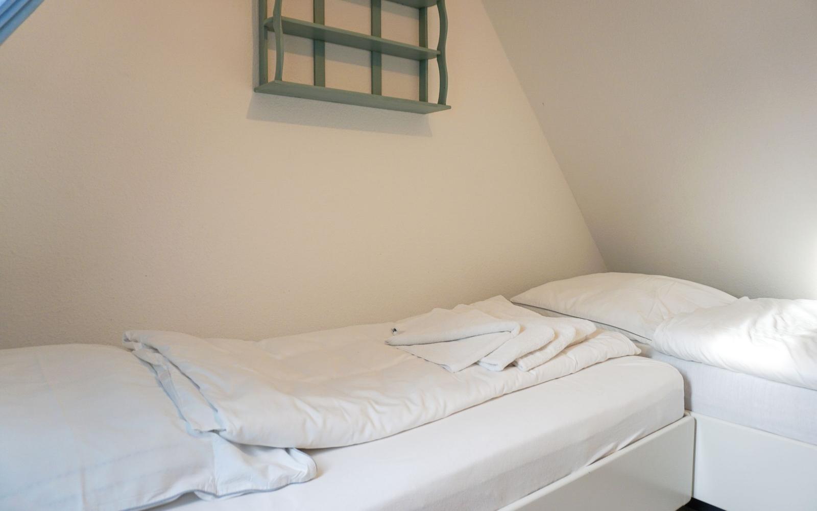 Two beds with white linens and towels against sloped walls.