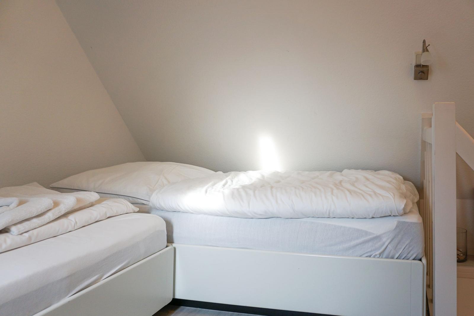 Room with two beds and slanted walls. Lighting on the wall.