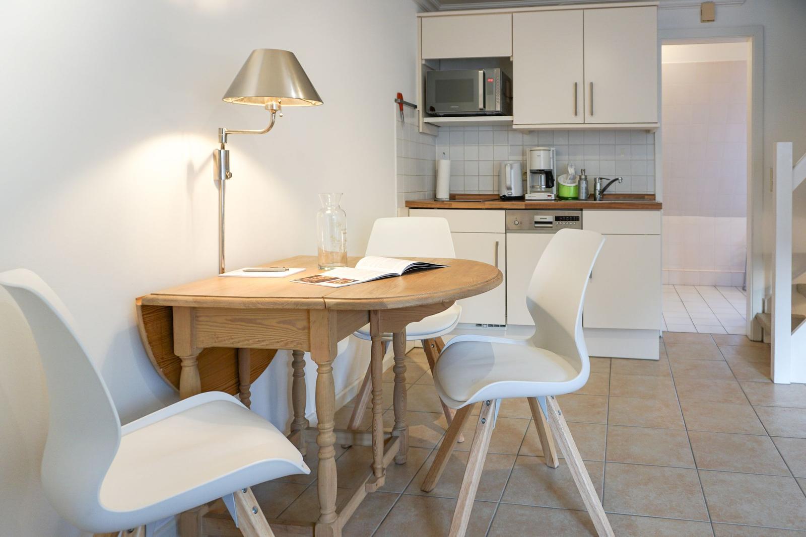 Dining table with three chairs and kitchen area in background.