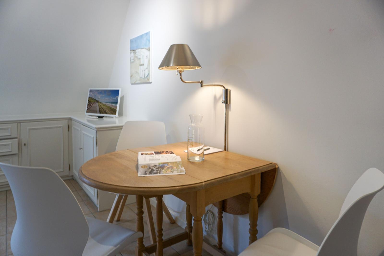 Wooden table with three white chairs, wall lamp, and picture on the wall.