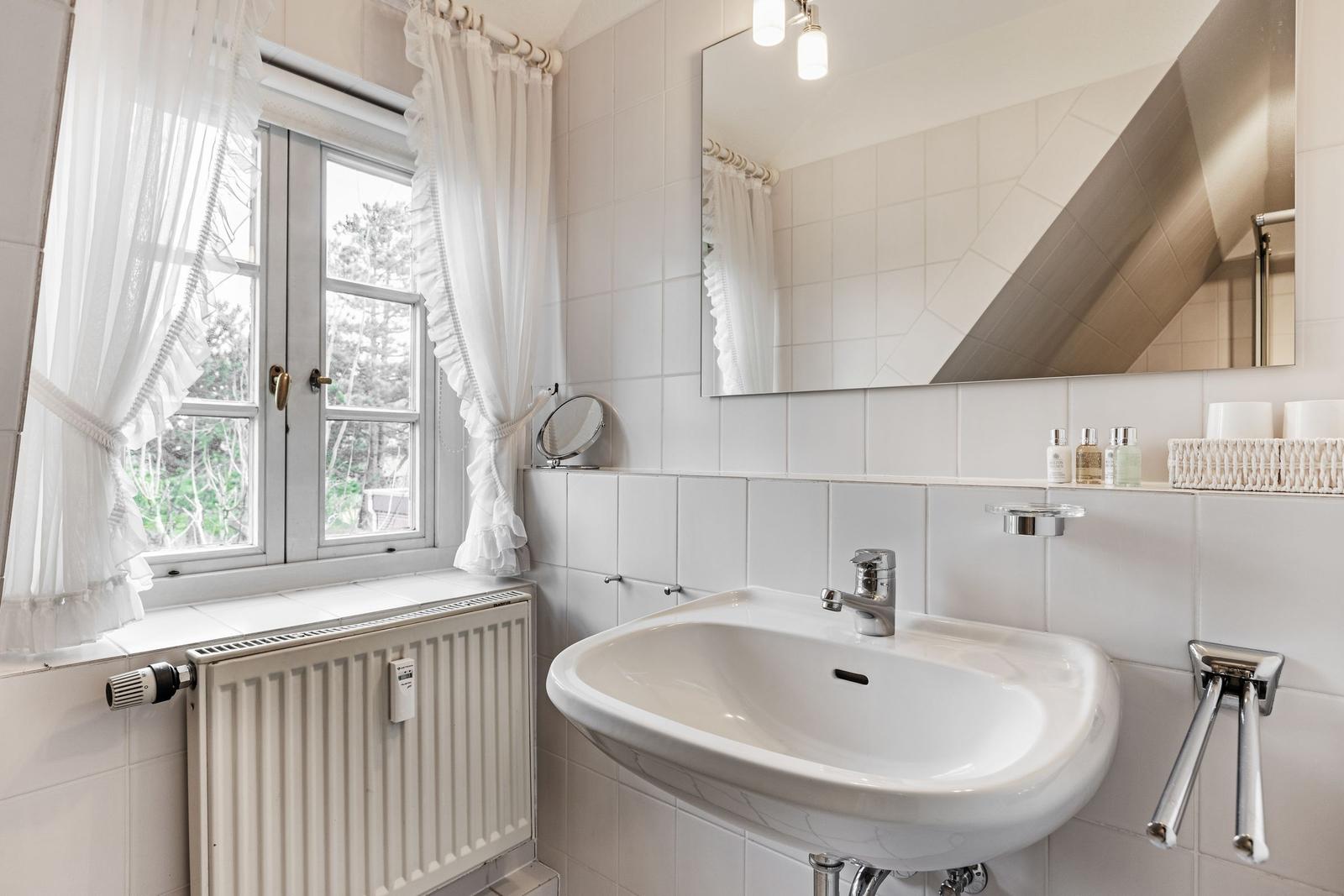 Bathroom with sink, mirror, and window with white curtains.