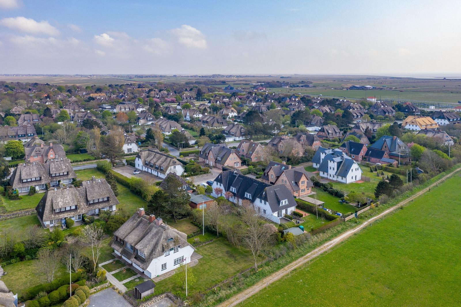 Aerial view of a village with thatched roofs and green fields.