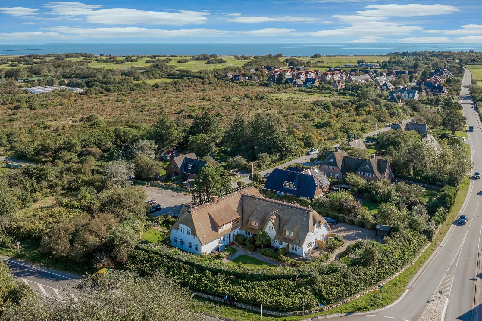House with thatched roof in green surroundings, view of sea and village.