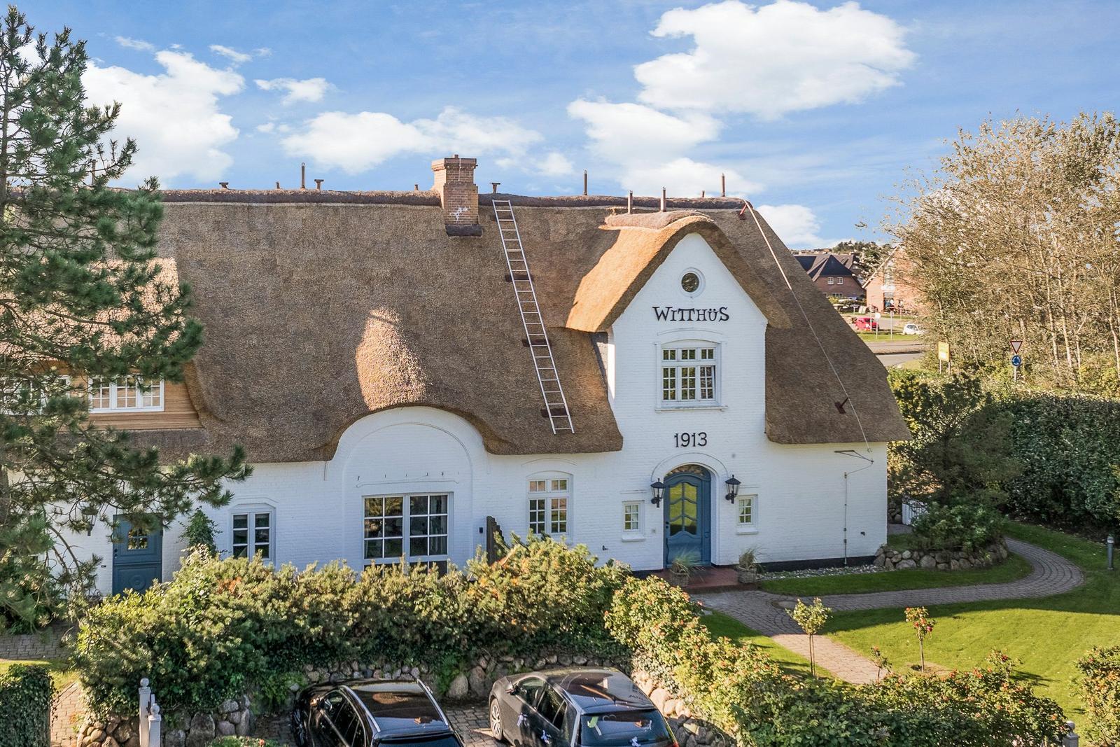 White house with thatched roof and blue door. Garden and parking visible.
