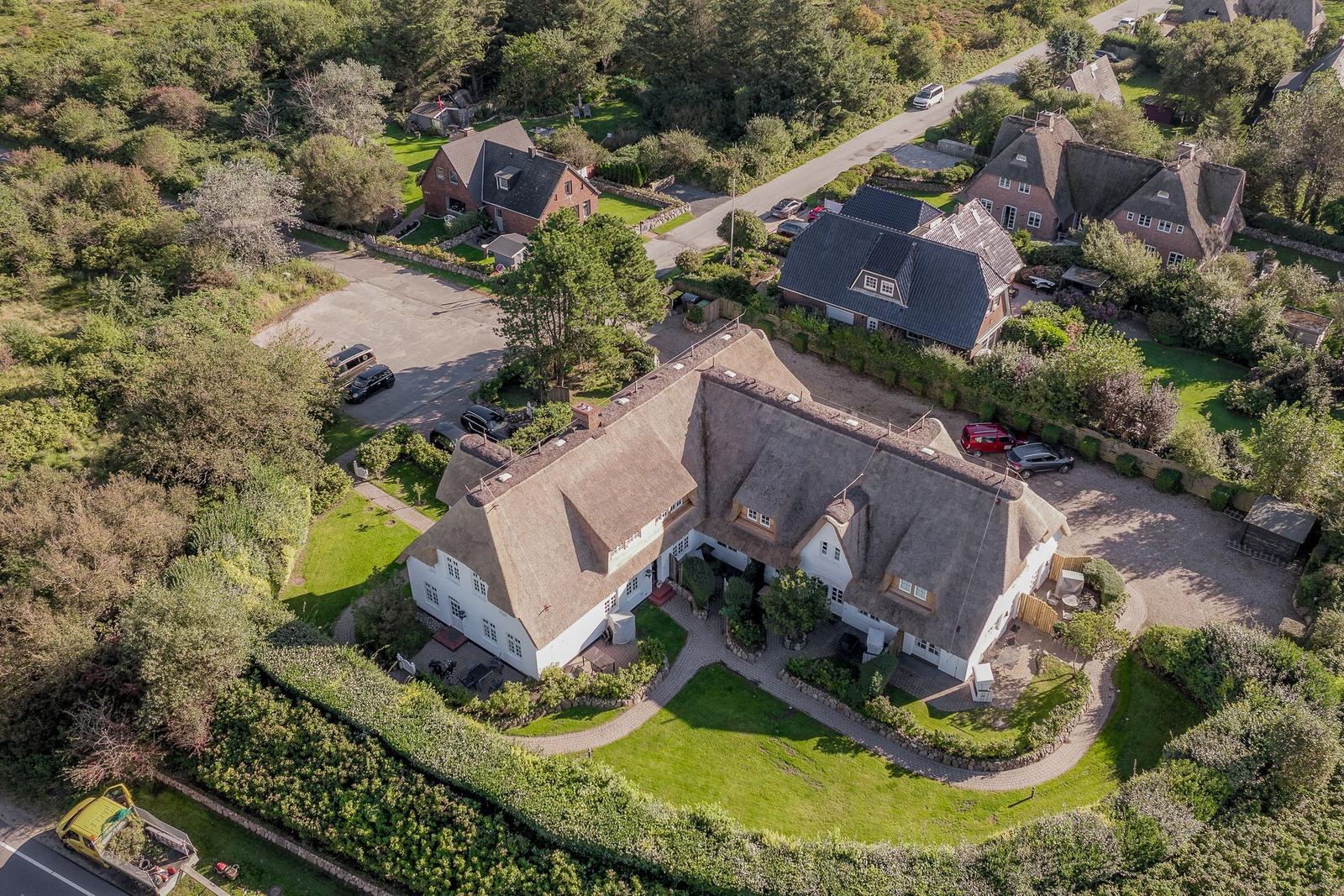 House with thatched roof, surrounded by green areas and paved paths.