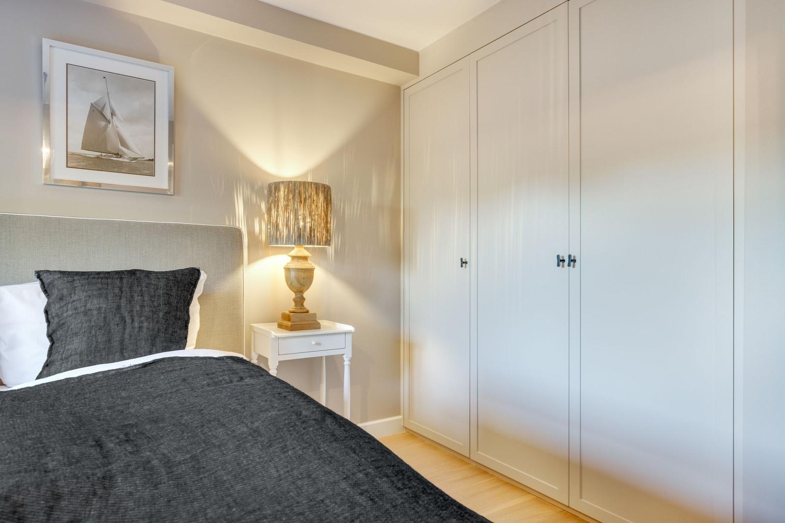 Bedroom with bed, nightstand, and wardrobe. Wall art and lamp are visible.