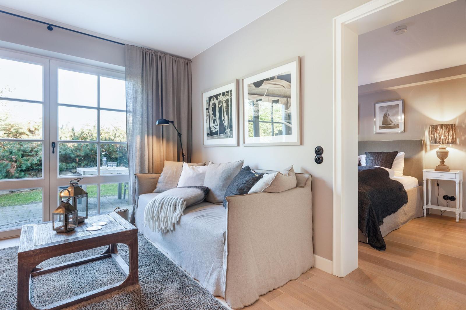 Living area with sofa and garden view. Adjacent room with bed and nightstand.