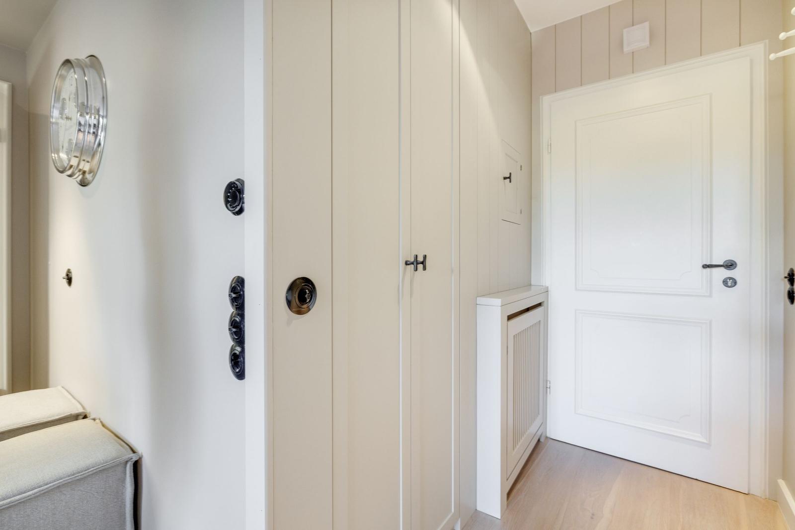 Hall with closet, door, and wall clock. Wooden floor and neutral wall color.