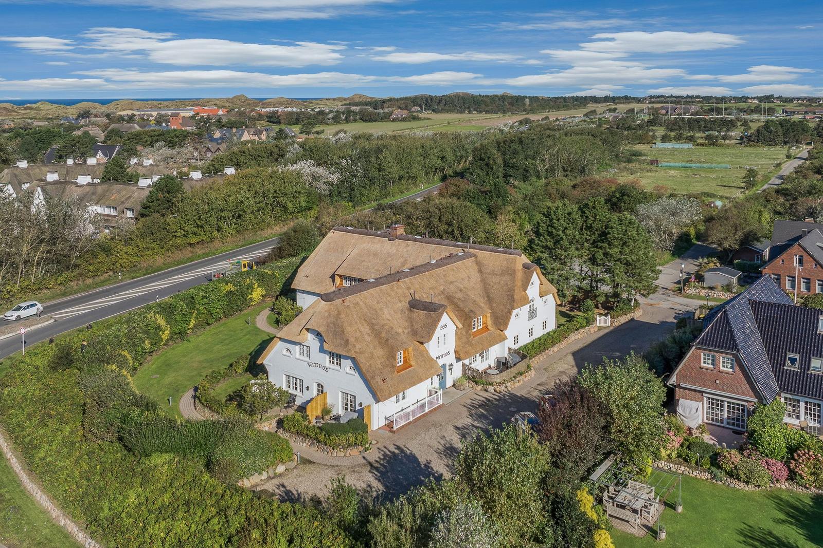 Farmhouse with thatched roof, surrounded by green fields and forest.
