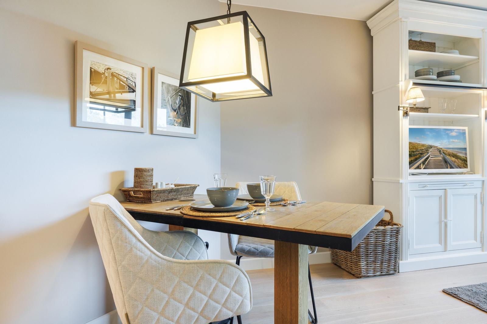 Dining room with wooden table, chairs, and pendant lamp. Pictures hang on the wall.