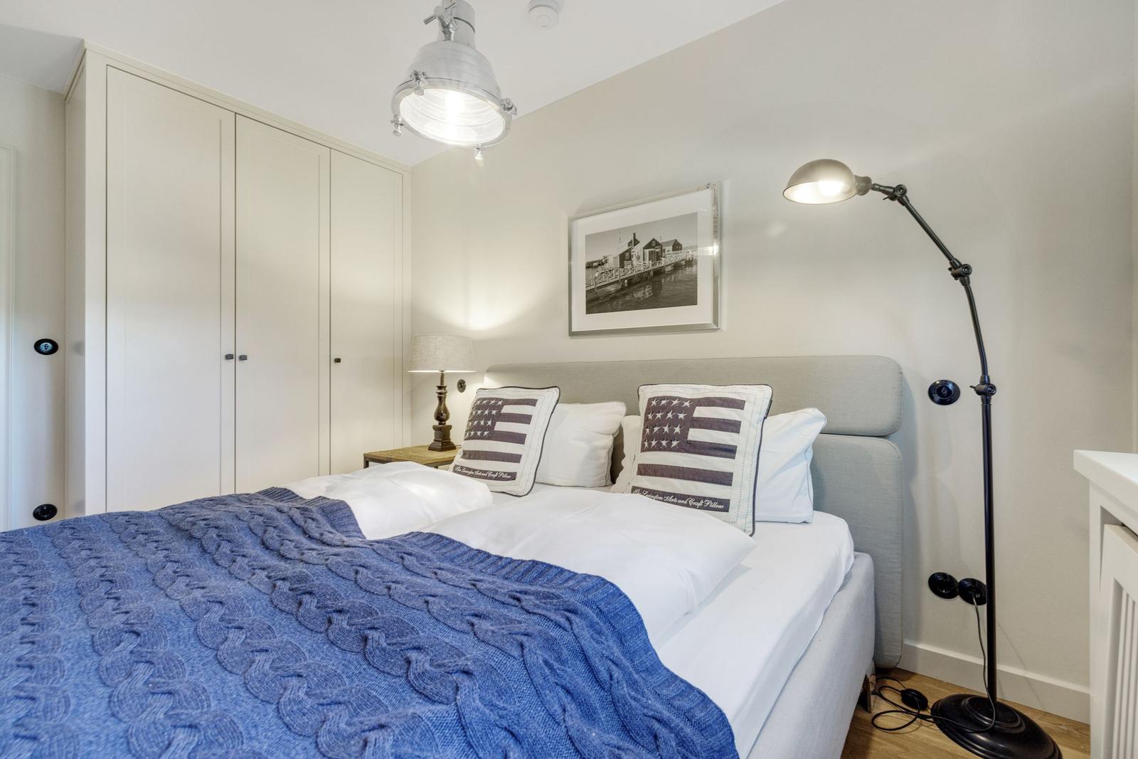 Schlafzimmer mit Bett, Kleiderschrank und Stehlampe.