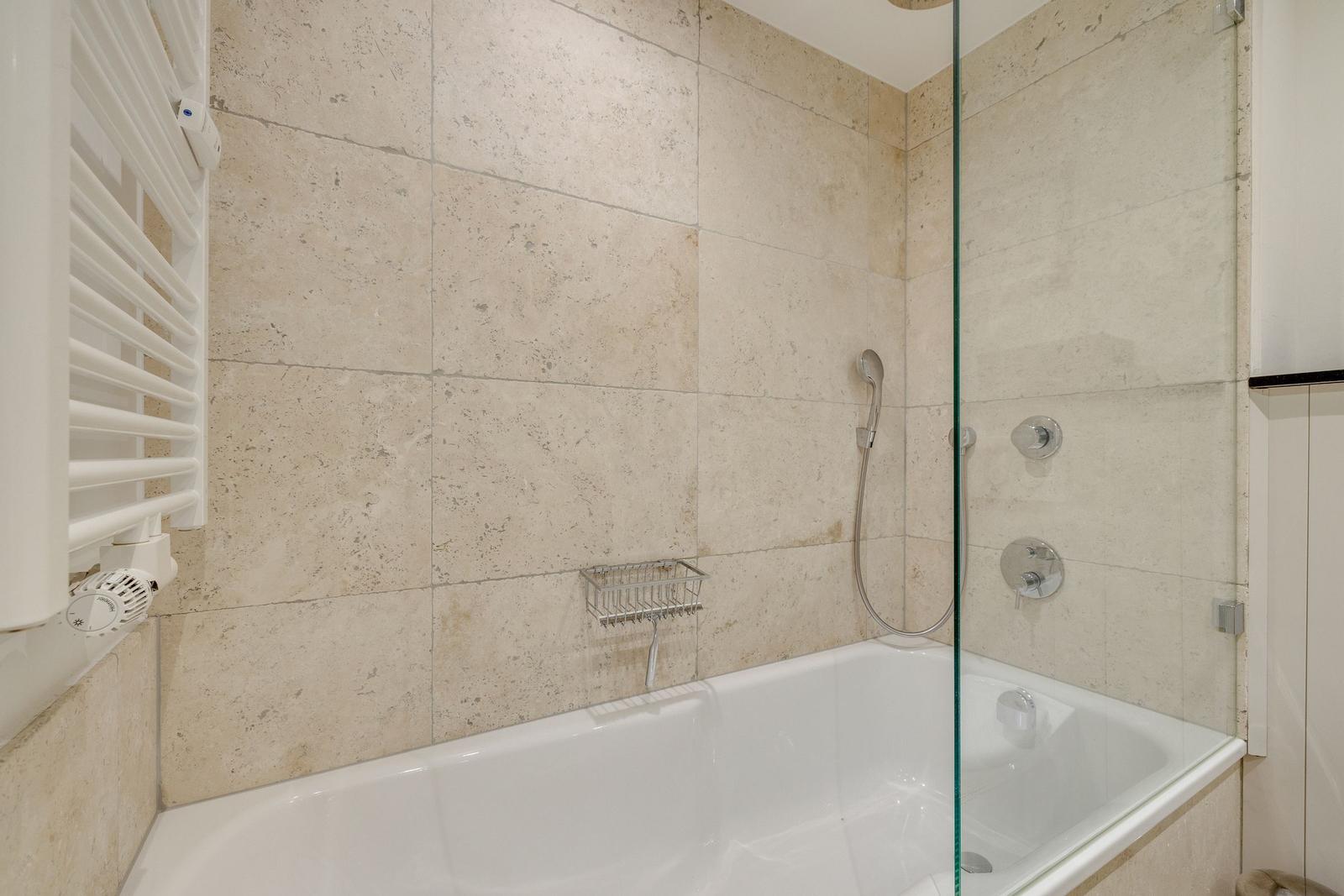 Bad mit Dusche und Badewanne, belegt mit Steinplatten und Glaswand.