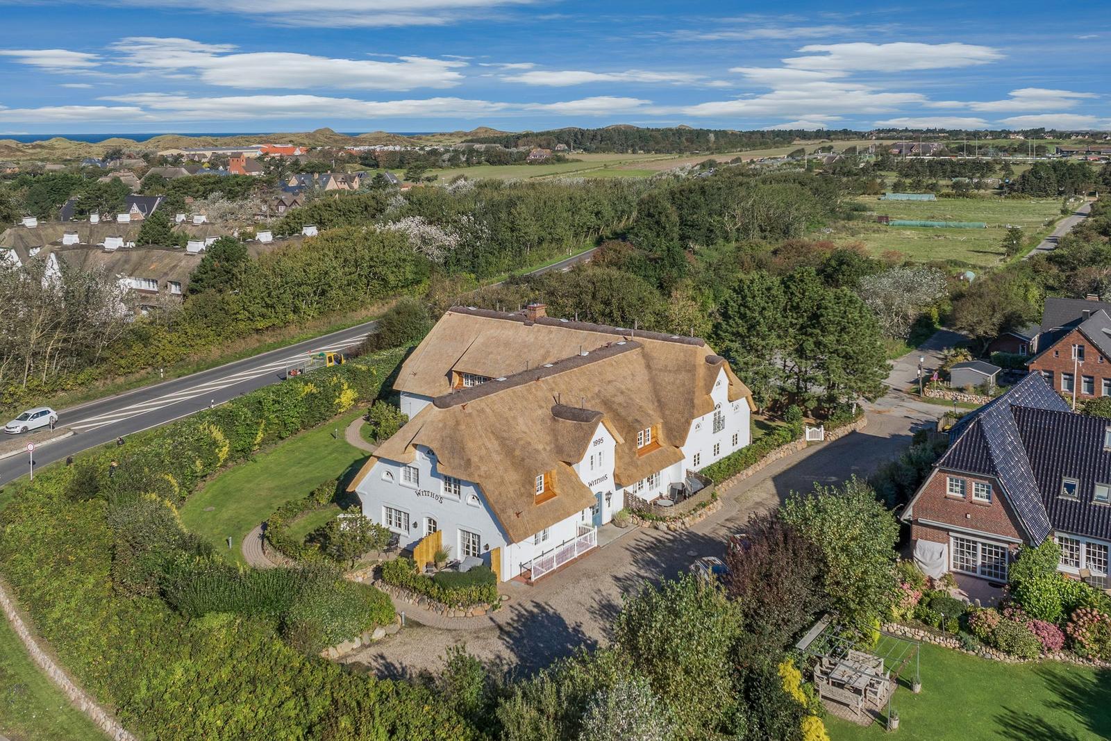 Haus mit strohgedecktem Dach und Garten, umgeben von Wald und Feldern, mit Blick auf das Meer.