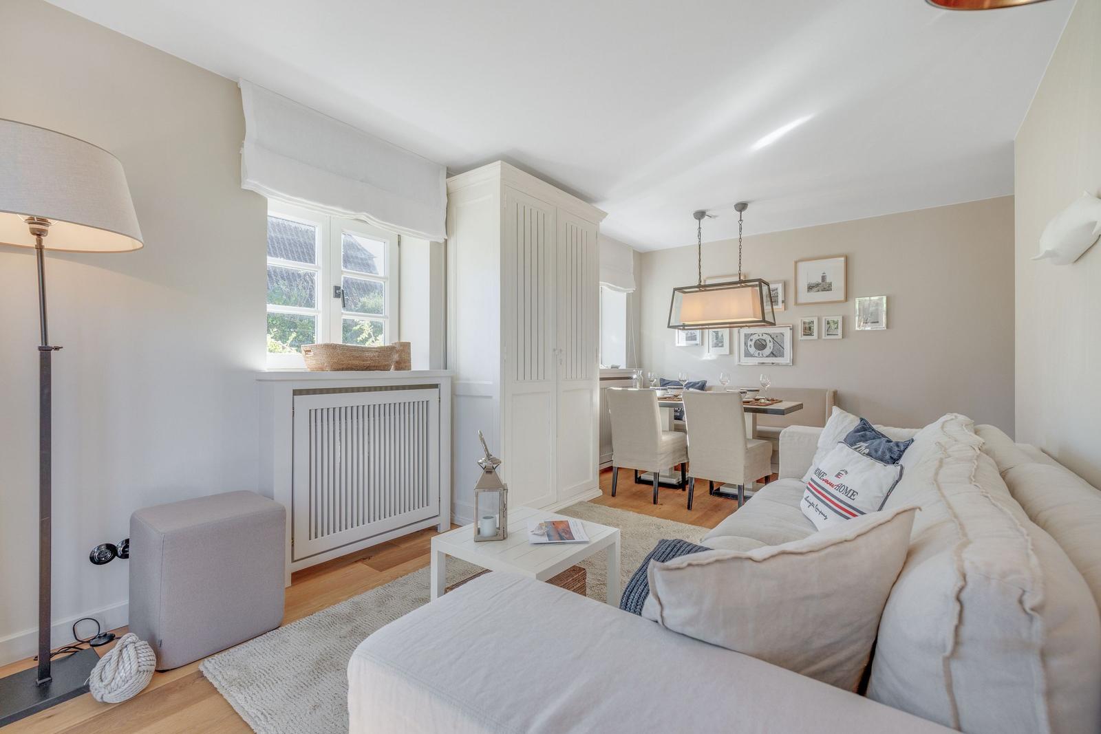 Wohn- und Essbereich mit Sofa, Tisch und Stühlen. Fenster und Wanddekoration sichtbar.