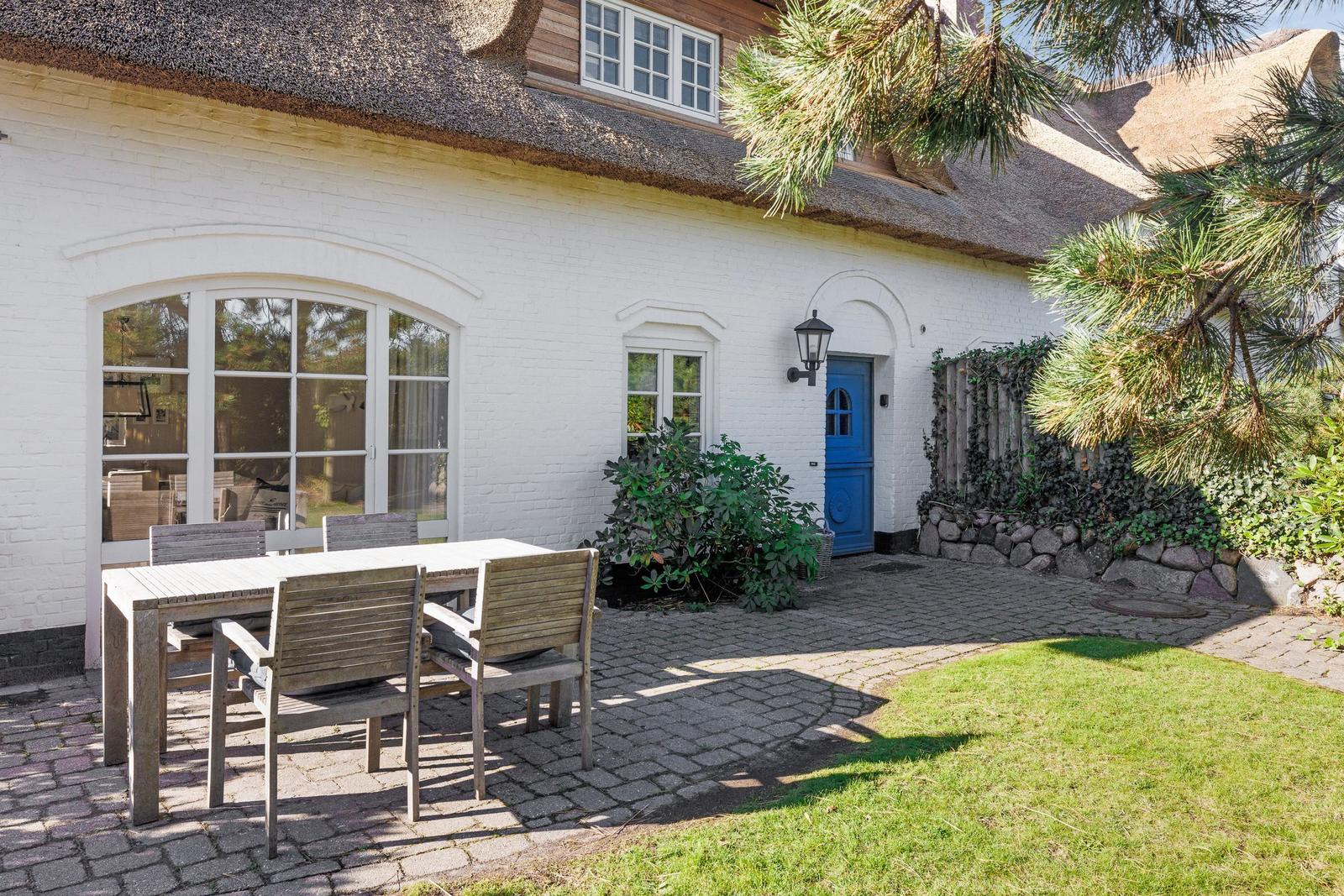 Wohnhaus mit strohgedecktem Dach und blauer Tür. Außenbereich mit Tisch und Stühlen.