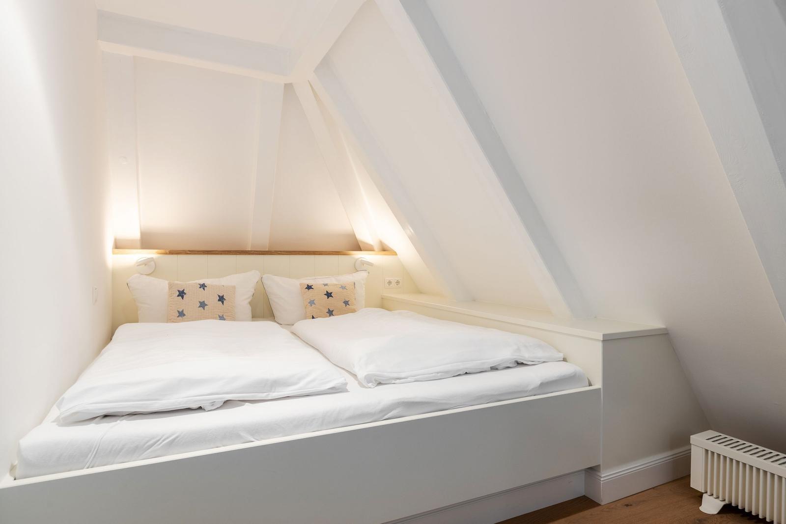 Doppelbett unter Dachschrägen mit weißen Laken und Kissen mit Sternenmuster.