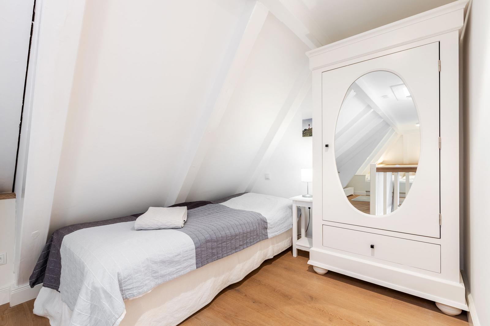 Schlafzimmer mit Dachschräge, weißem Schrank mit Spiegel und Bett mit grauem und weißem Bettzeug.