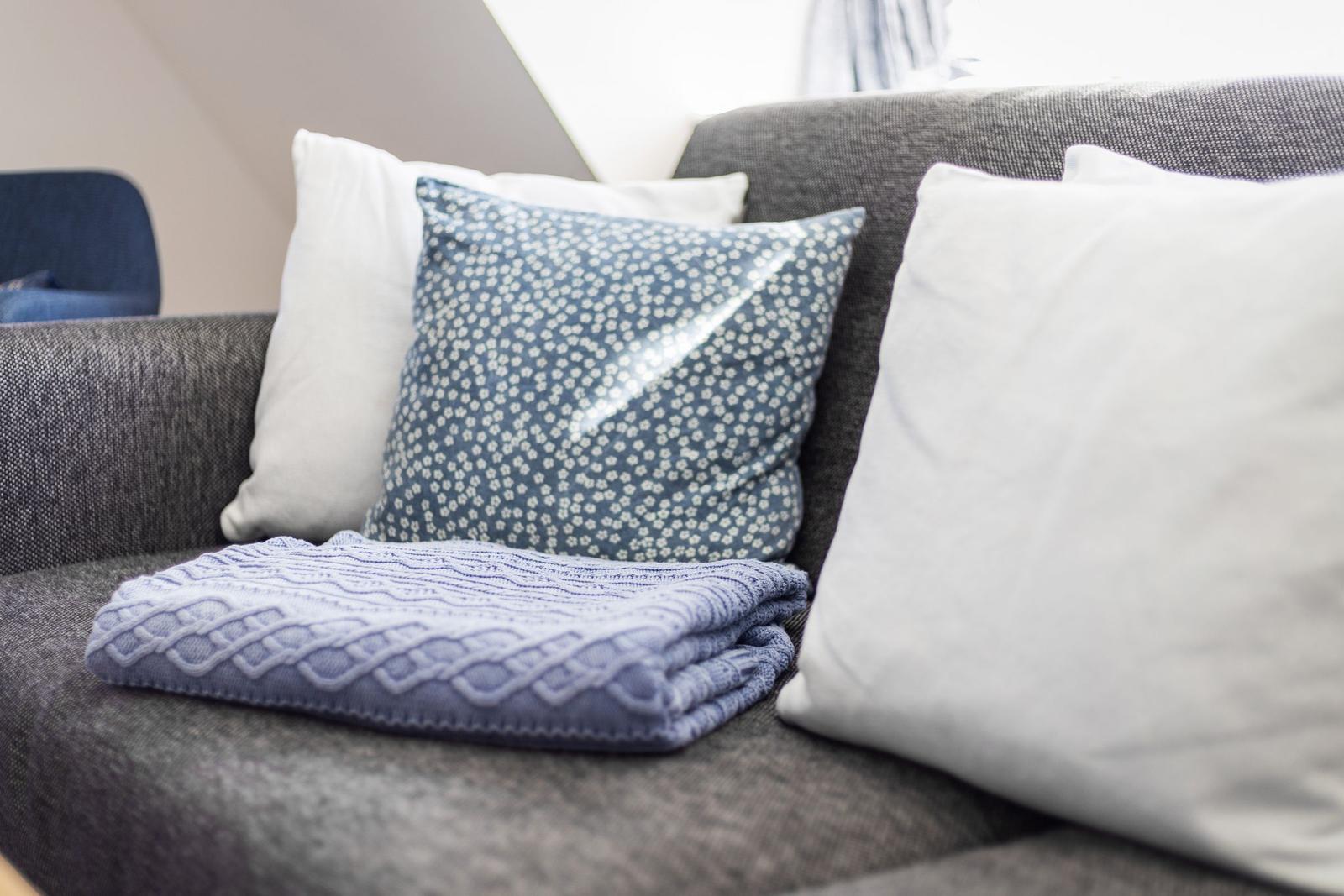 Ein grauer Sofa mit Kissen und einer Decke.
