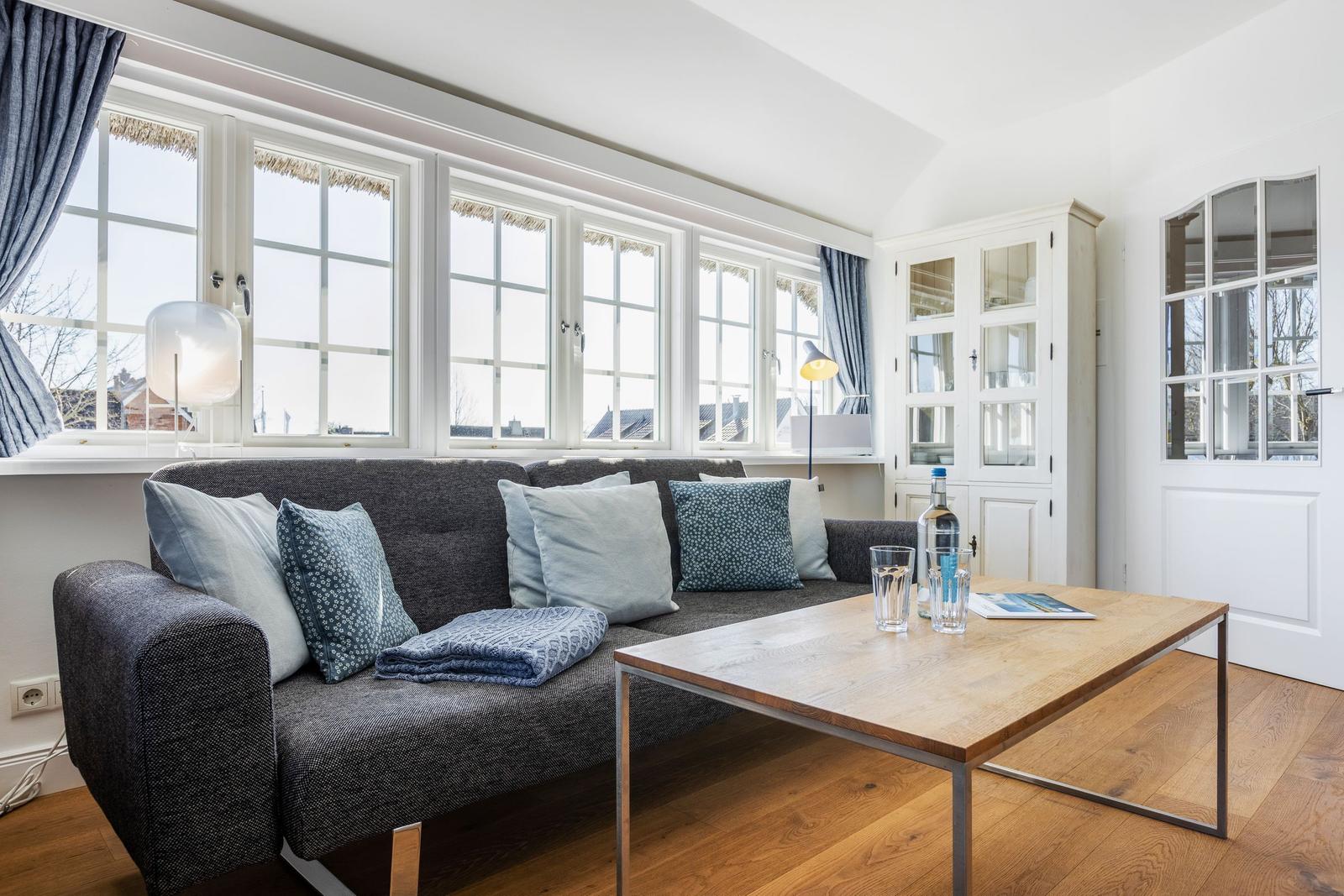 Ein Wohnzimmer mit Sofa, Tisch und Fenstern.