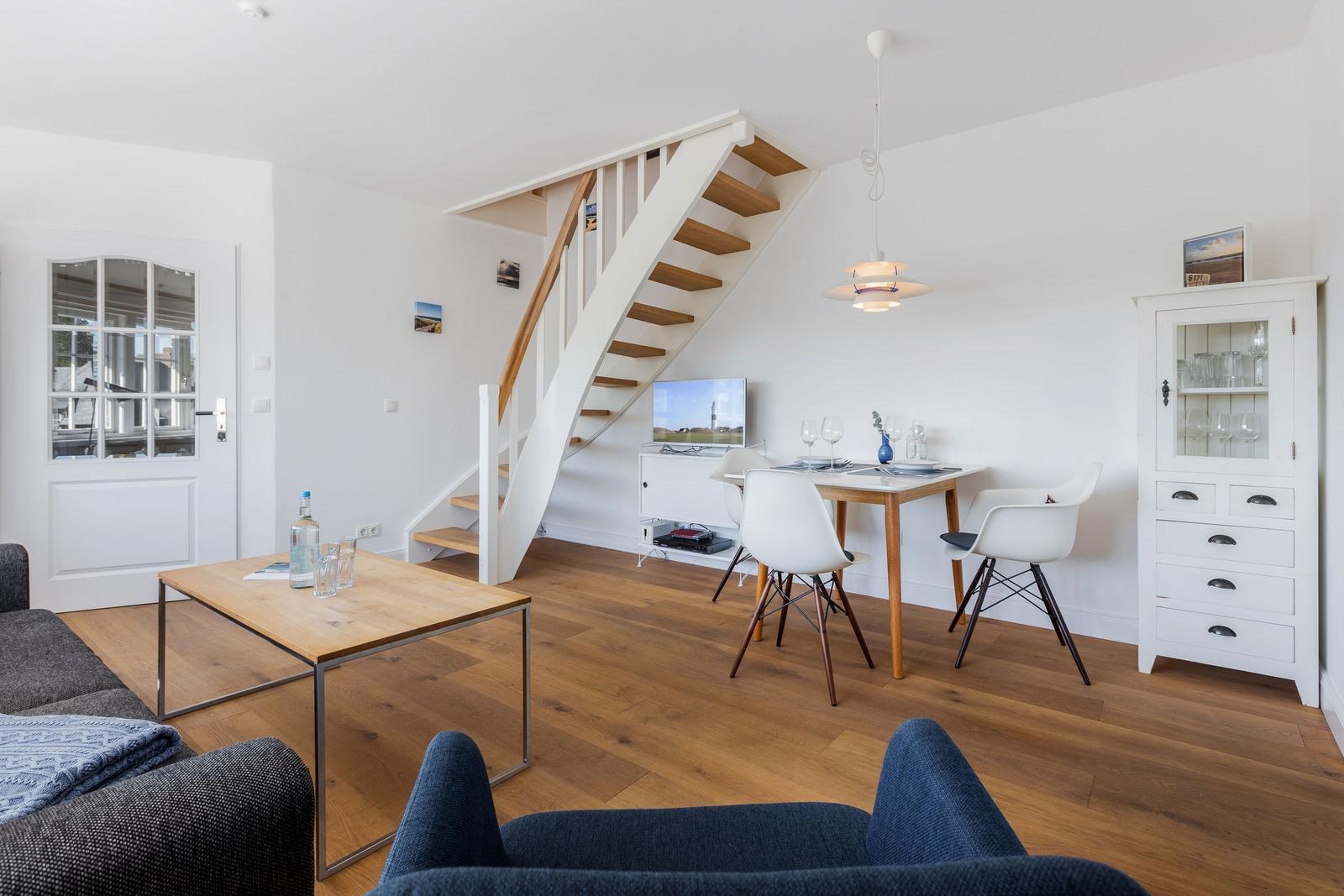 Wohn- und Essbereich mit Holzboden, Treppe und weißer Einbauküche.