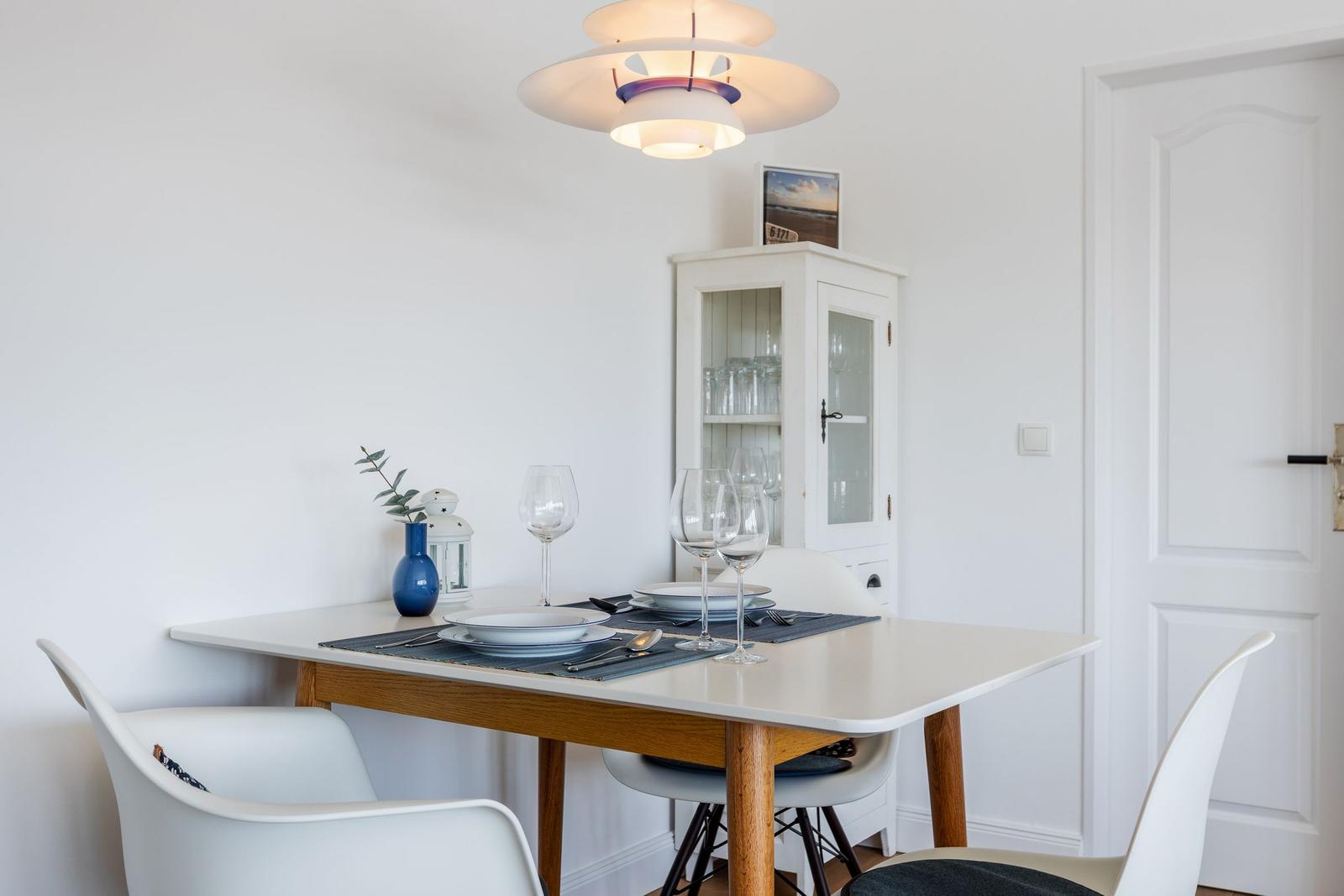 Esstisch mit Stühlen, Glas- und Porzellanbesteck, Vase und Decke.