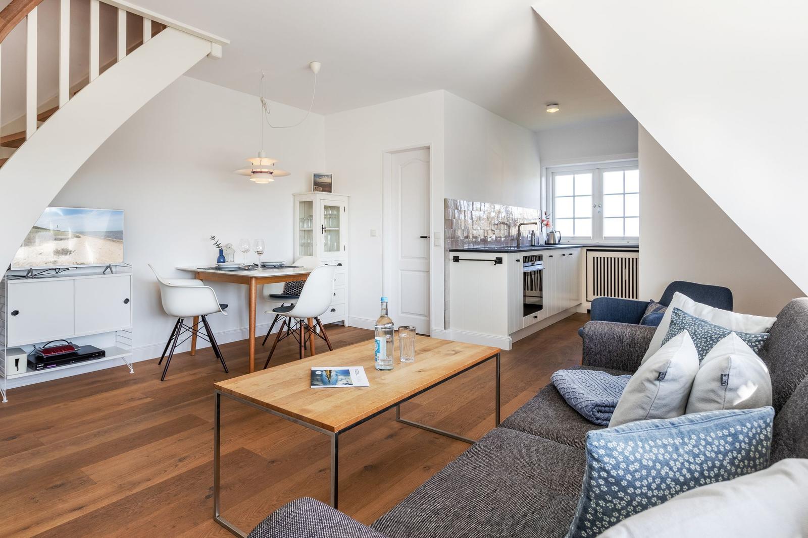 Wohnbereich mit Sofa, Esstisch, Küche und TV unter Dachschrägen.