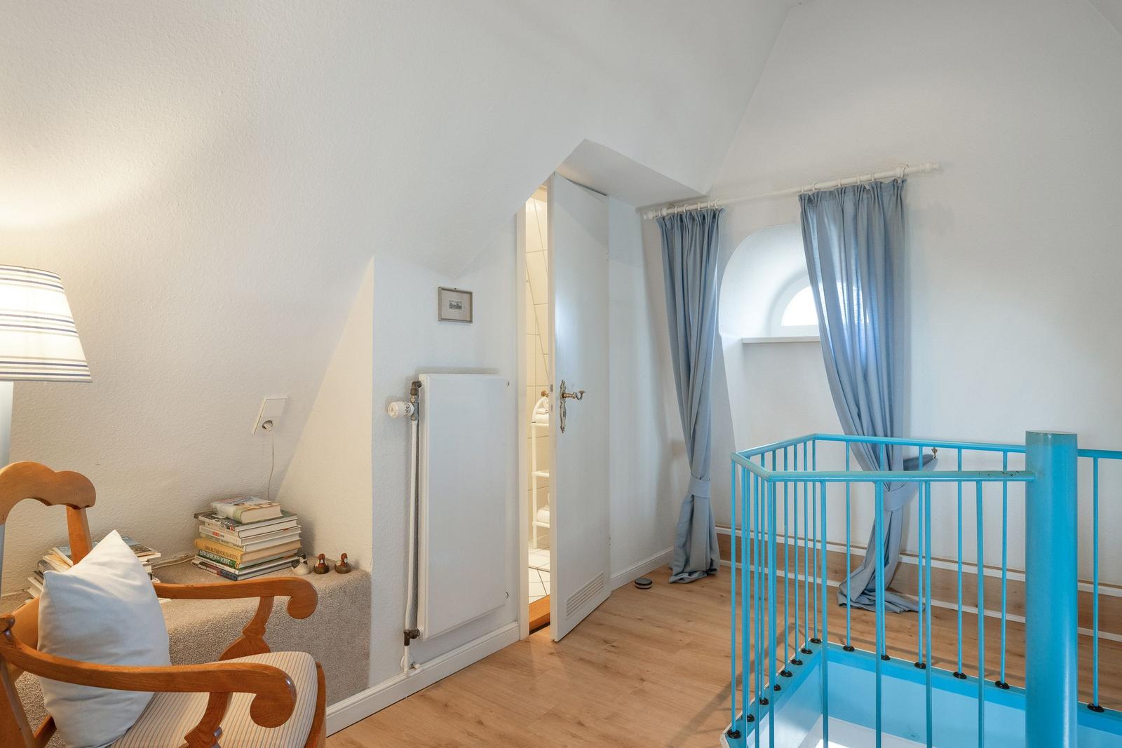 Schlafzimmer mit Holzboden, blauer Babygitter, Bücher und Tür zur Dusche.