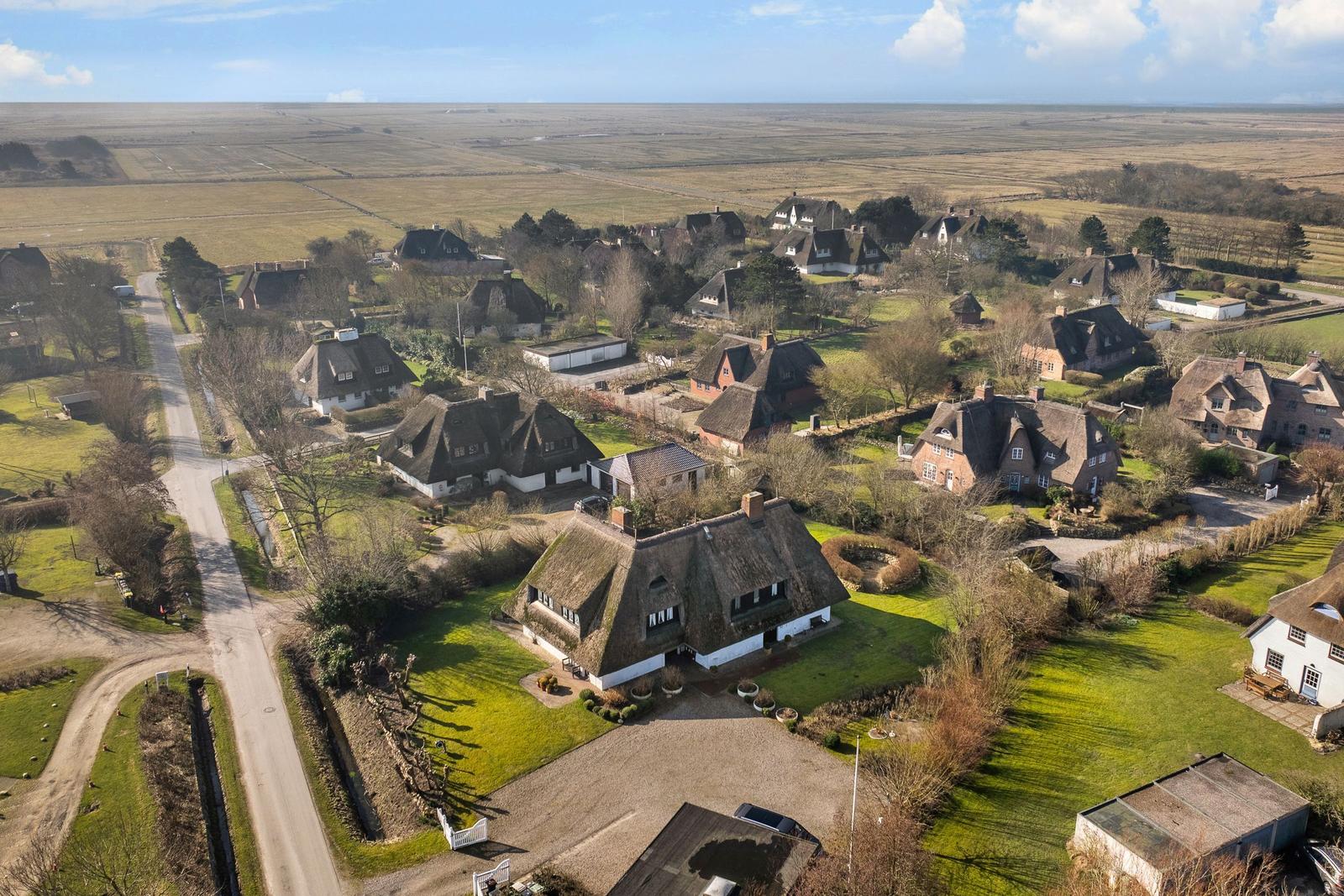 Dorf mit strohgedeckten Häusern und grünen Wiesen unter blauem Himmel.