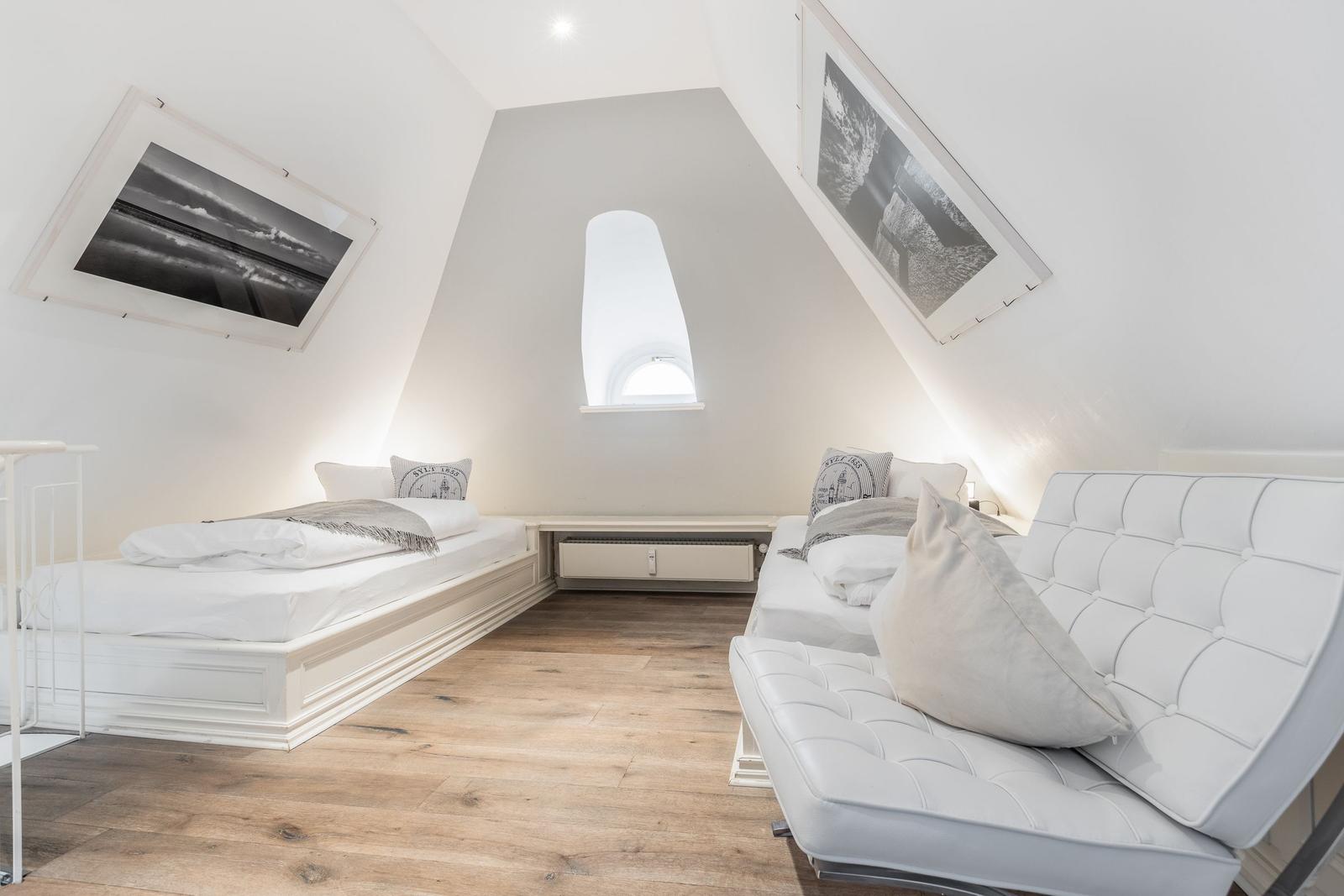 Room with two beds and sofa under sloped ceilings. Wooden floor and window.
