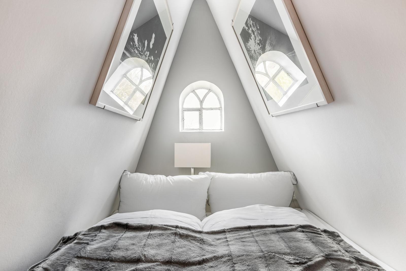 Bedroom with sloped ceilings, three windows, and white bed.