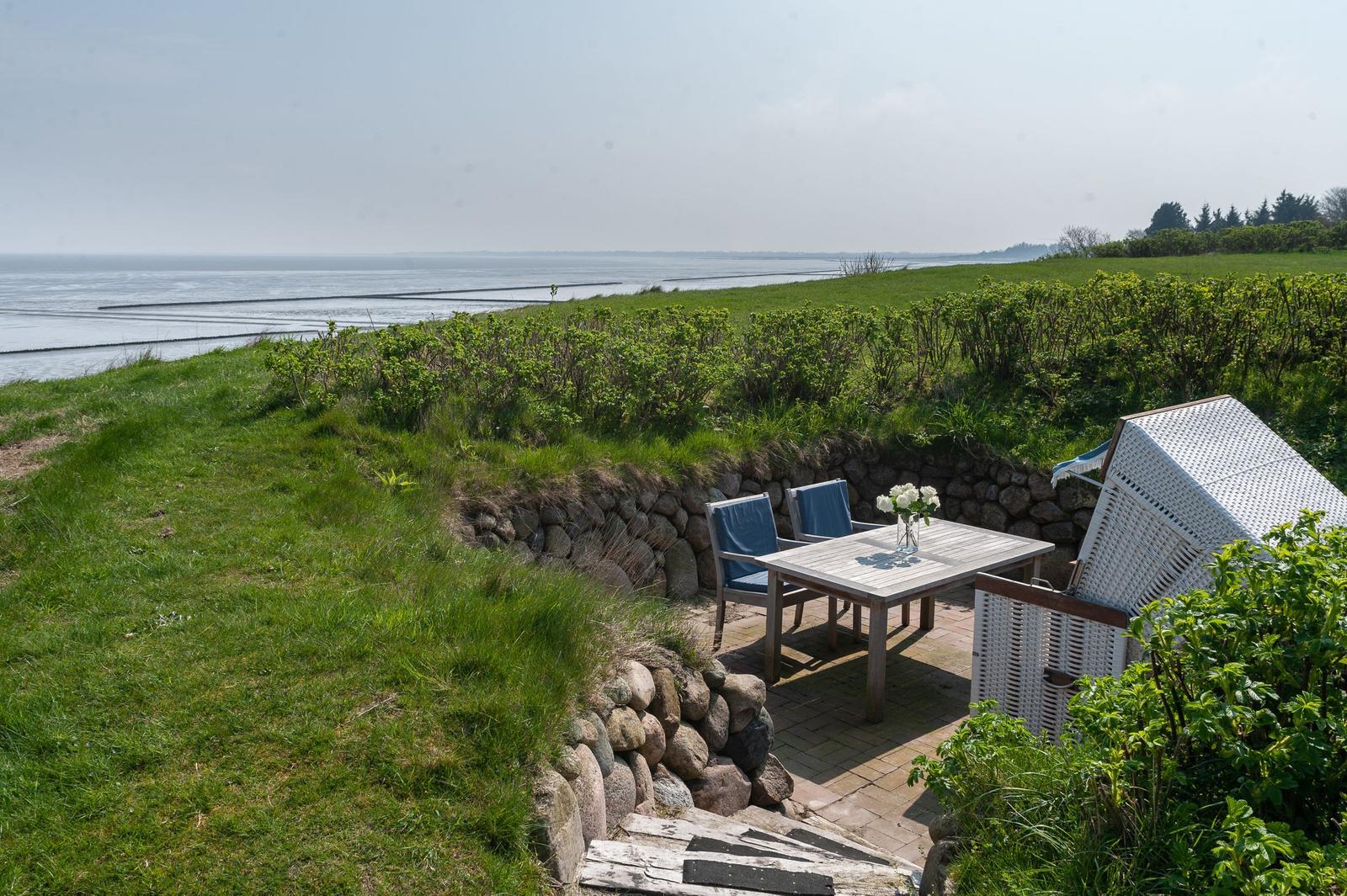 Terrasse mit Tisch und Stühlen, Blick auf das Meer und grüne Wiesen.