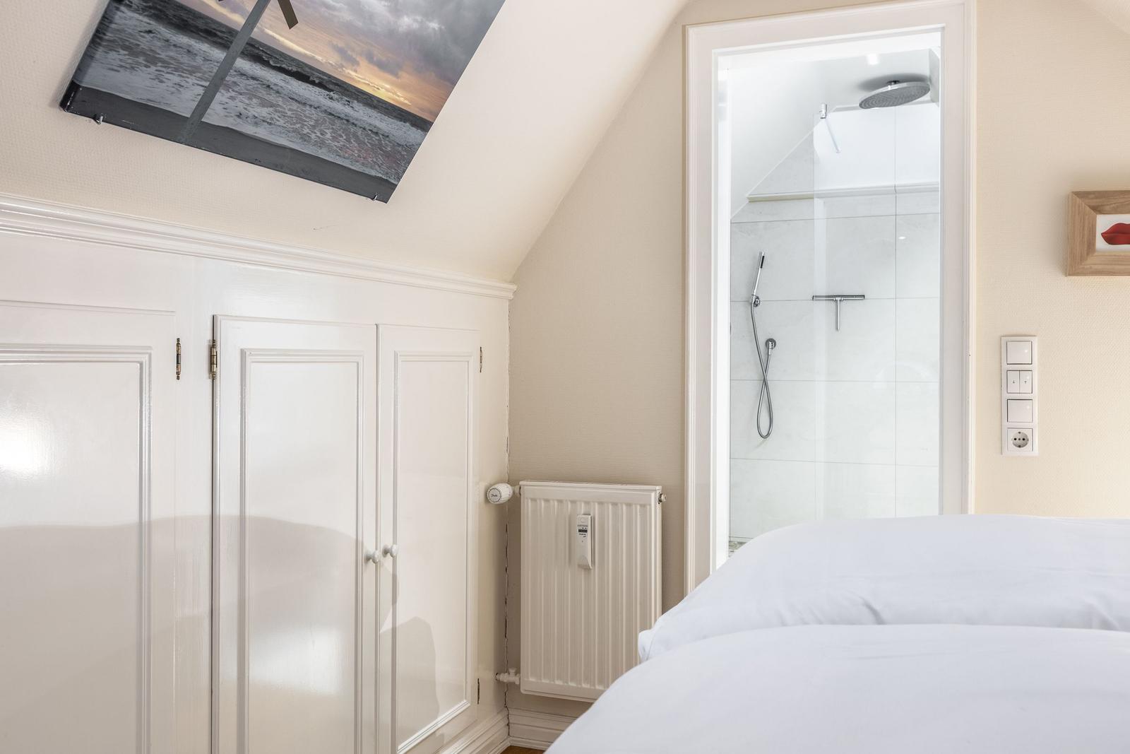 Schlafzimmer mit Dachschrägen, weißer Einbauschränke und Blick in Dusche.