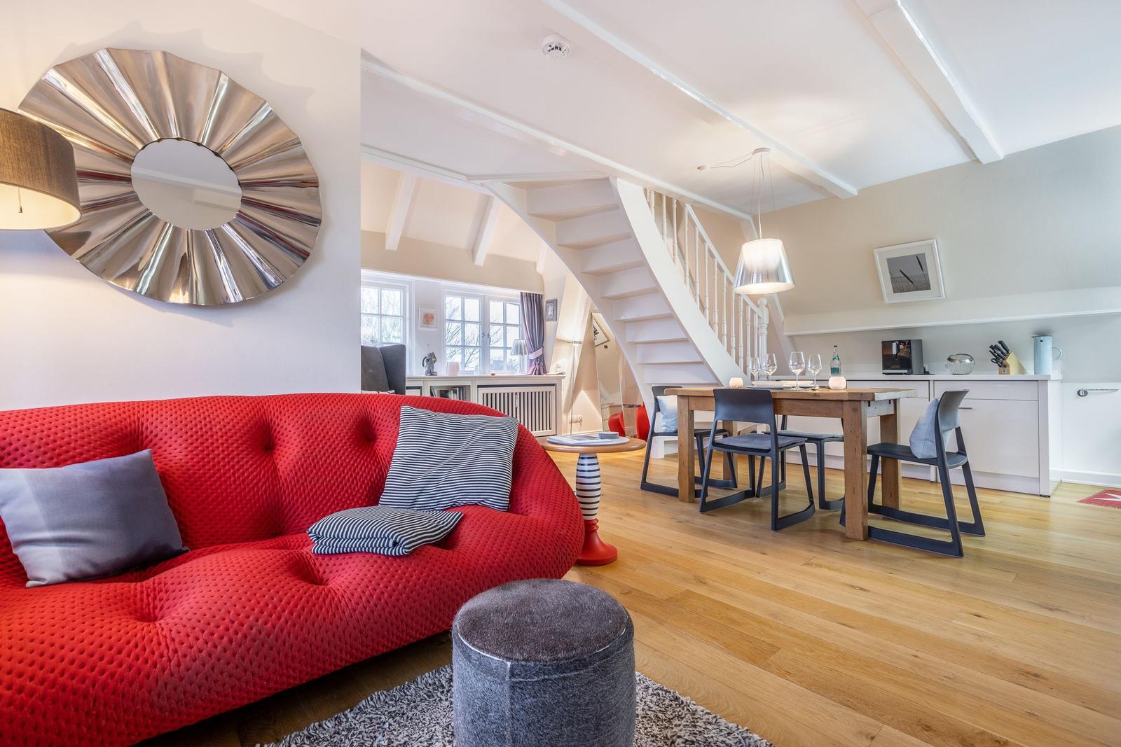 Roter Sofa, Esstisch mit Stühlen, weiße Treppe und Holzboden.
