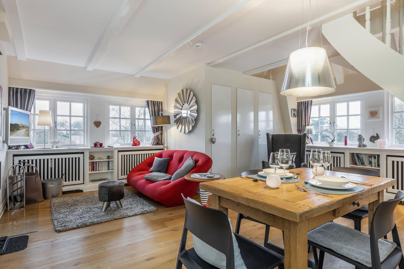 Wohn- und Essbereich mit rotem Sofa, Holztisch und großen Fenstern.